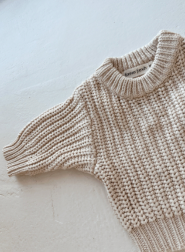 A close-up of the Cream | Knit Sweater by forever french baby, featuring chunky ribbed texture, short sleeves, and soft cotton fabric. Laid flat on a white surface with a visible neckline tag.