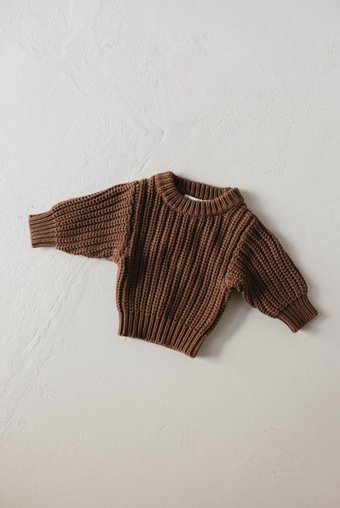 The forever french baby Hot Cocoa Knit Sweater, a small brown long-sleeve baby sweater, is displayed flat on a light textured surface.