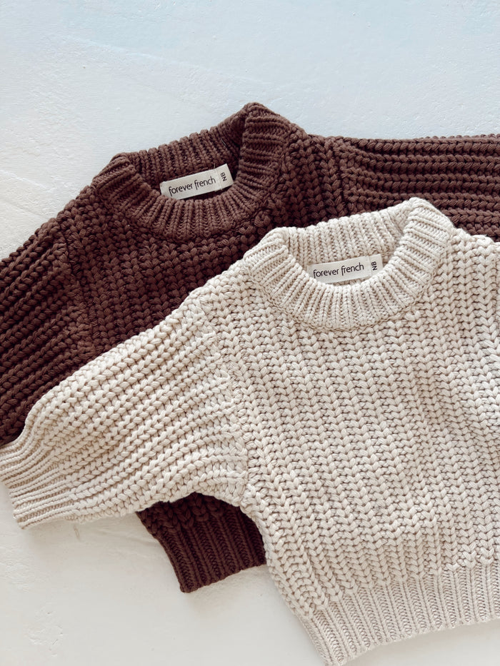 Two chunky Hot Cocoa | Knit Sweaters by forever french baby, in dark brown and cream, are laid flat on a white surface. Both cotton sweaters feature ribbed collars, cuffs, hems, and “forever french” labels at the neck.