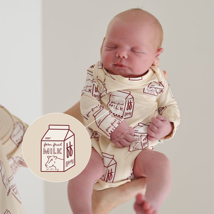 A newborn wears the forever french baby Long Sleeve Bamboo Snapsuit | Milk in cream, featuring cartoon milk cartons. An inset shows the "gluten free milk" design, highlighting this soft, hypoallergenic snapsuit for sensitive skin.
