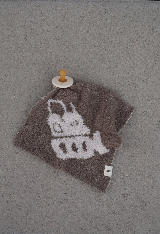 A brown "Lovey | Bulldozer" by forever french baby featuring a white cartoon bulldozer design rests on a gray surface, with a beige pacifier with brown nipple attached to one corner.