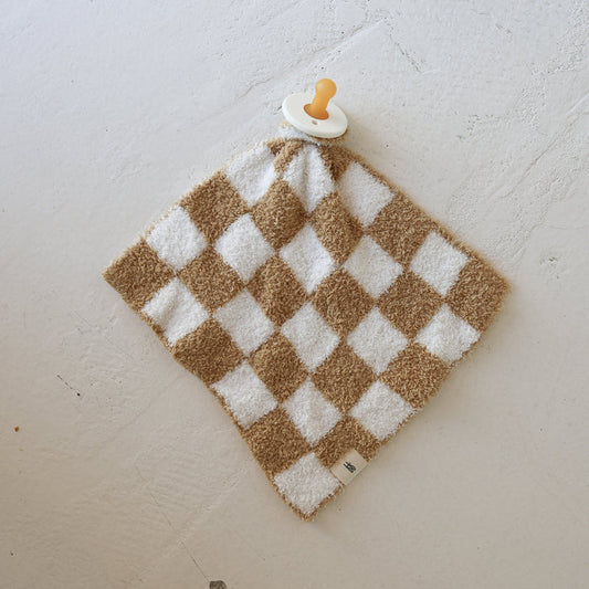 The Lovey | Original Checkerboard from forever french baby, a plush microfiber baby blanket with a beige and white checkered pattern and attached pacifier, rests on a textured white surface.