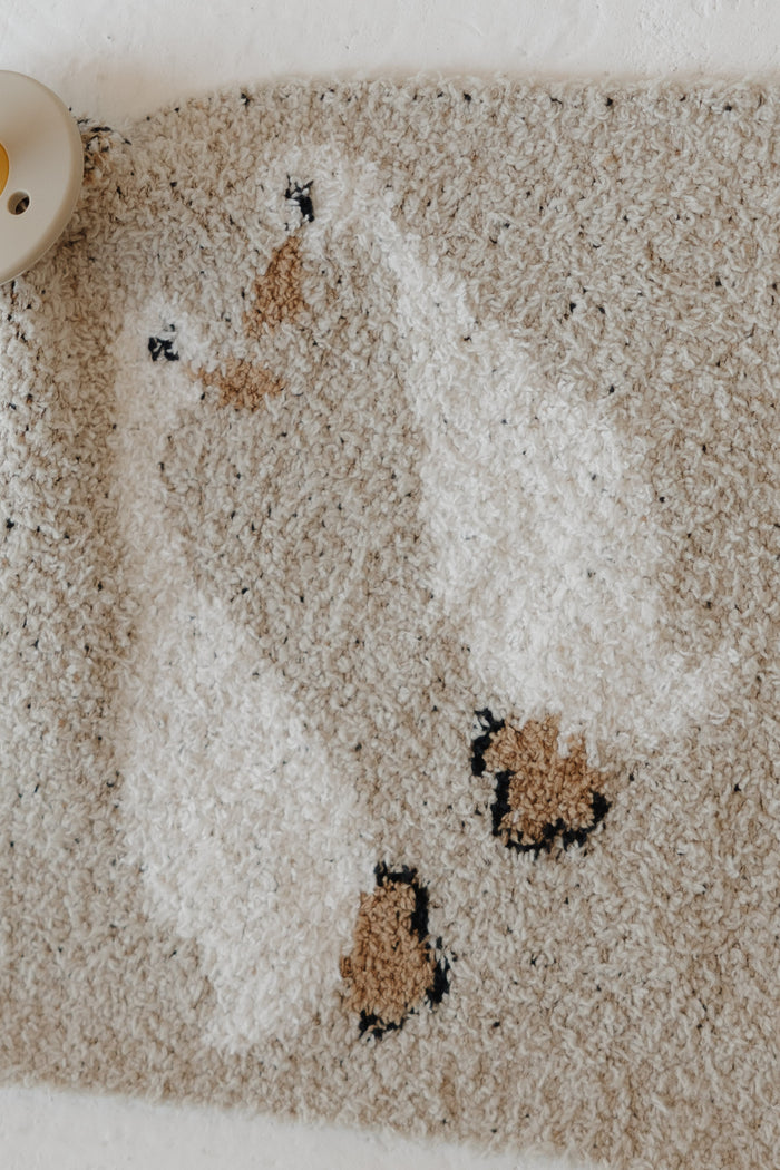 A close-up of the Lovey | Silly Goose by forever french baby—a textured beige microfiber feather yarn rug with two white ducks, brown beaks and feet, plus a beige pacifier partly shown in the top left corner.