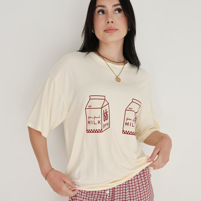 A woman models the forever french baby Short Sleeve Women's Bamboo Lounge Set | Milk & Window Pane, featuring a cream milk carton T-shirt and red windowpane pants, against a white background, gazing slightly upward.
