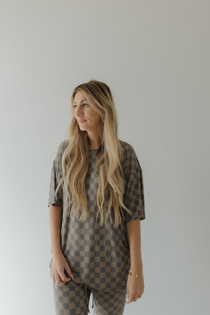 A person with long blonde hair poses against a plain background, wearing an oversized Short Sleeve Women's Bamboo Pajama in Faded Checkerboard by forever french baby. The hypo-allergenic set's relaxed fit complements their serene gaze to the side.