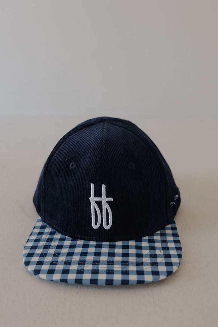 The Snapback | Blue Corduroy ff by forever french baby features a navy blue corduroy design, blue and white checkered brim, adjustable fit, and a white "ff" embroidered logo. Displayed on a plain light background, it combines comfort and style.
