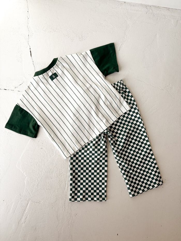 The forever french baby T-Shirt & Pant Set | Lucky Micro Check is displayed on a light surface, featuring a short-sleeve shirt with green sleeves and black pinstripes, paired with green checkerboard kids wide leg pants.