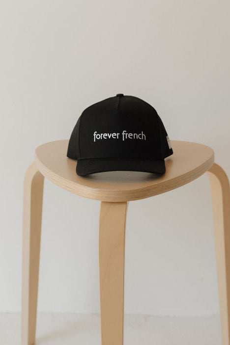 The Snapback | forever french Black by forever french baby is displayed on a wooden stool, set against a plain, light-colored background.