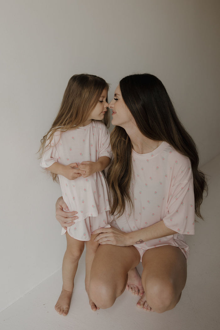 A woman kneels beside a young girl, both dressed in matching forever french baby Women’s Bamboo Short Set | Rosie pajamas featuring delicate patterns. They gently touch noses and smile softly in a bright, minimalist room.