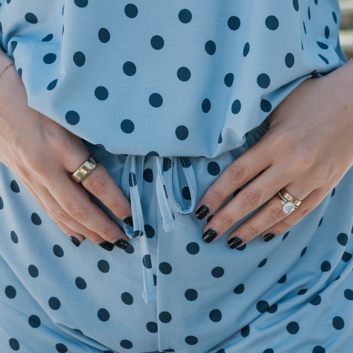 Close-up of hands with black nail polish and rings resting on a baby bump, featuring the Women's Bamboo Short Set | Sully by forever french baby — a soft, stylish, and hypo-allergenic blue polka dot pajama set.