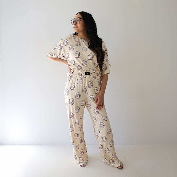 A woman with long dark hair and glasses stands against a white background, modeling the forever french baby Women's Boxy Tee Lounge Set | Milk, featuring a playful milk carton print for a cozy, stylish look.